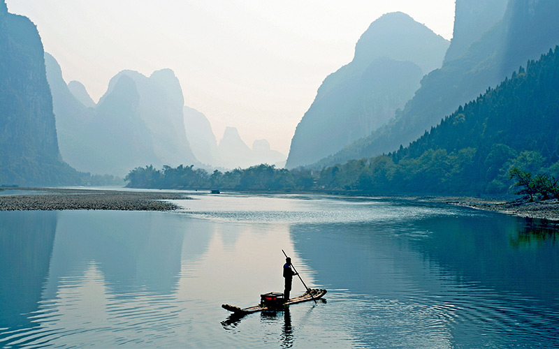 A man standing on a small boat in the middle of a lake in Guilin