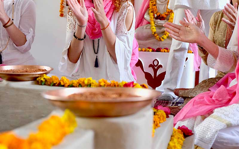 Ceremony with participants wearing white clothes and pink scarfs, surrounded by yellow flowers