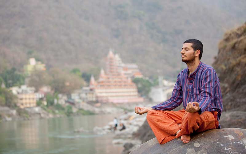 Man meditating on a rock overlooking a river town