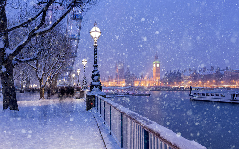 Snow falls over the River Thames in London at dusk