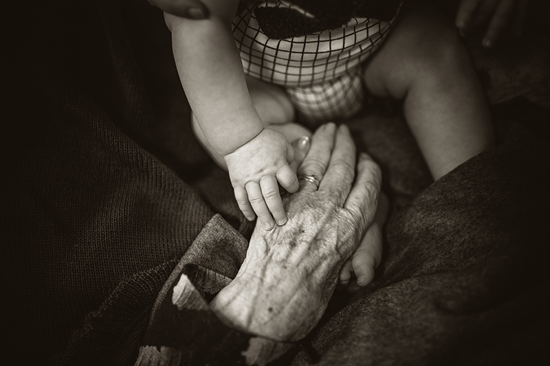 Elderly person and baby holding hands